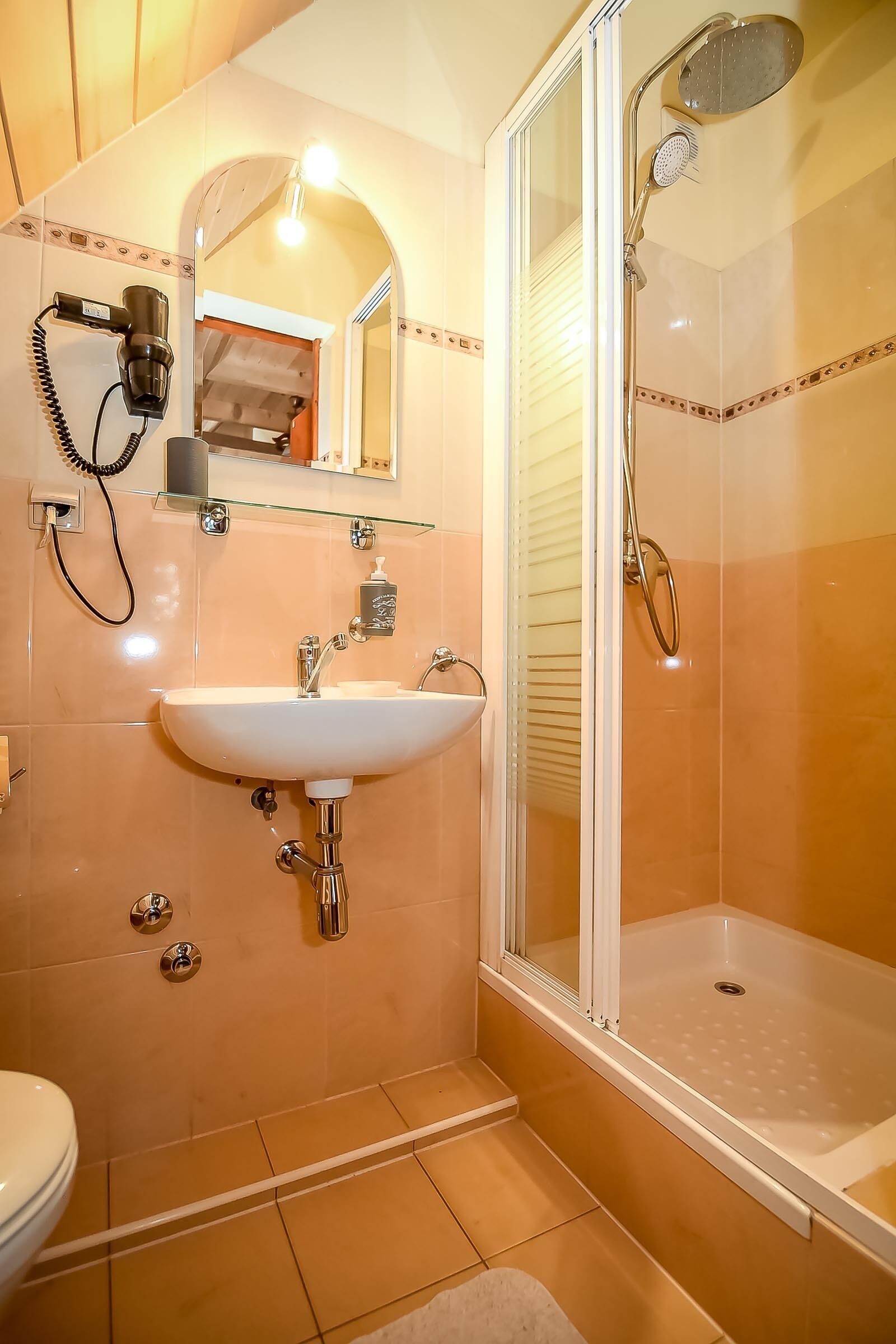 A bathroom with a white sink, a glass shower enclosure, and a hairdryer mounted on the wall.