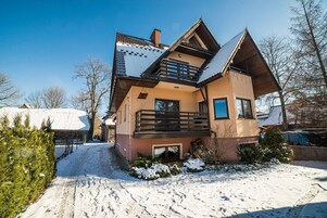 Una casa de dos pisos con un balcón, un tejado cubierto de nieve y un cielo despejado.