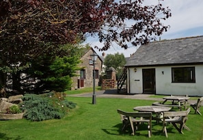 A courtyard with stone buildings, a wooden bench, and a small garden area. - Kennacott Court (Bude)