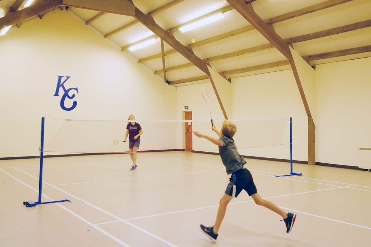 Un court de tennis intérieur doté d’un plafond haut et de poutres en bois.
