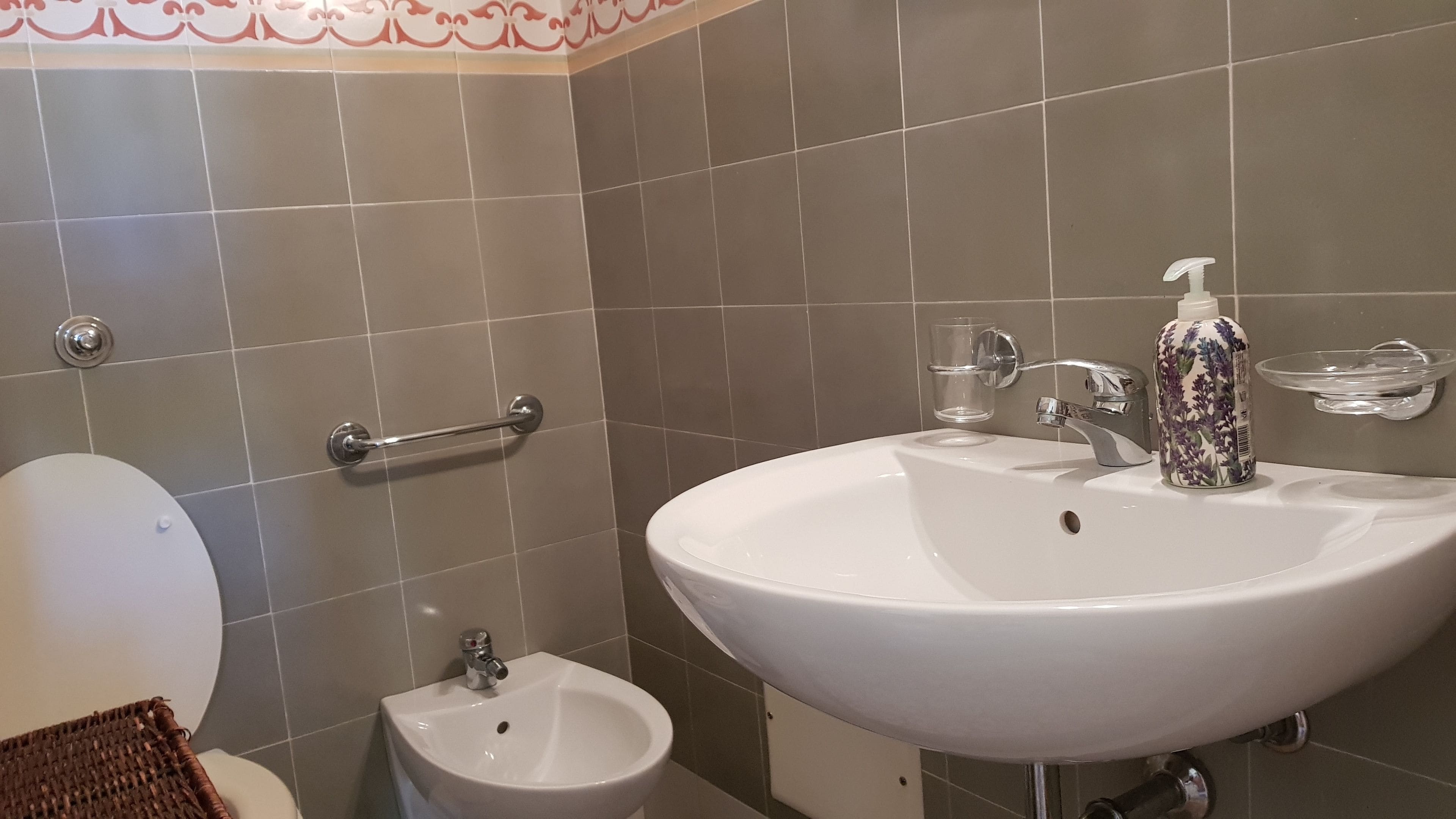 Un baño con lavamanos blanco, un bidé, un inodoro y un pasamanos.