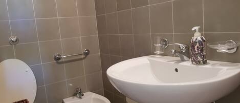 Un baño con lavamanos blanco, un bidé, un inodoro y un pasamanos.