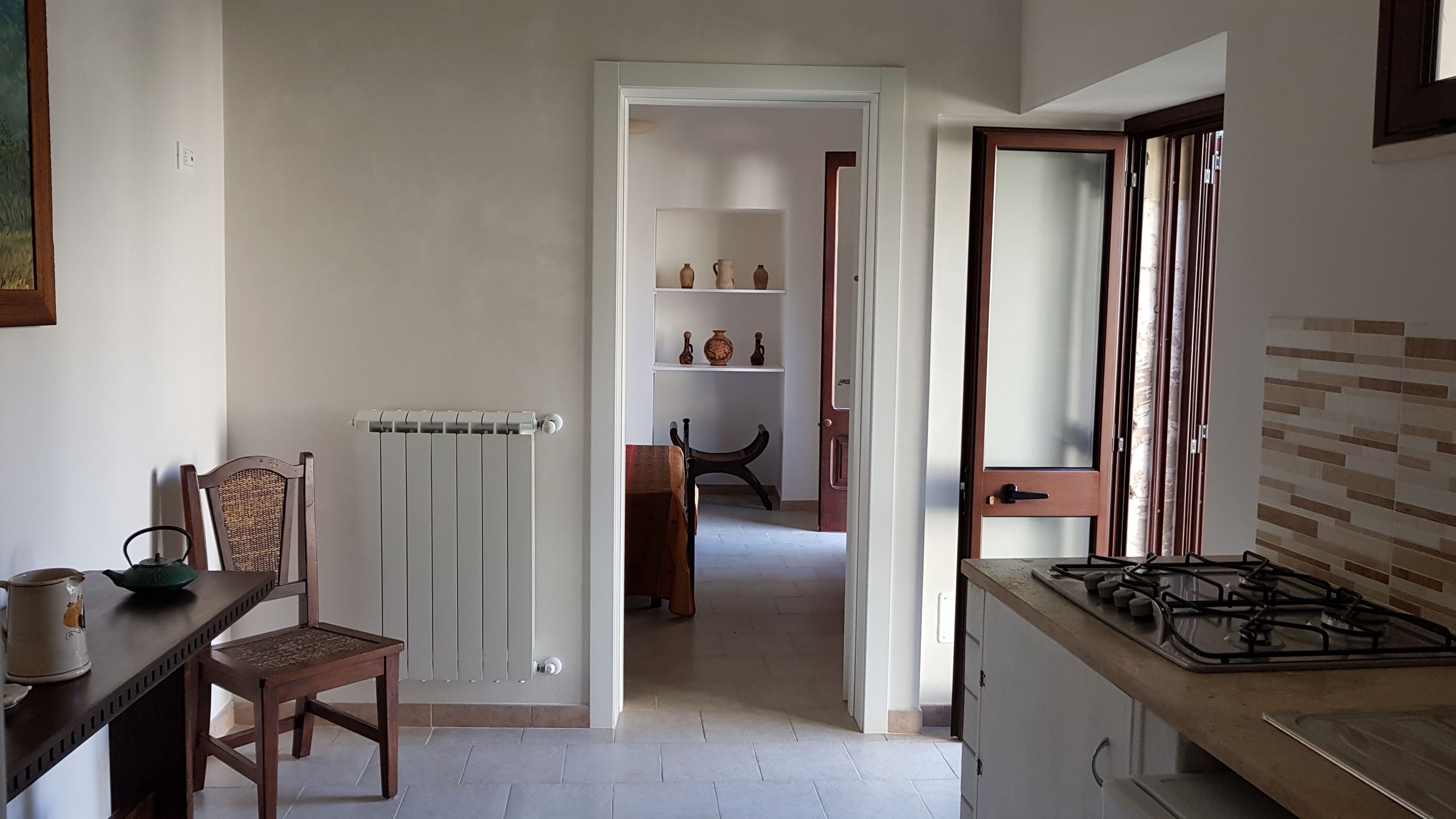 A kitchen with a gas stove, a radiator, a dining table with chairs, and a wooden chair.