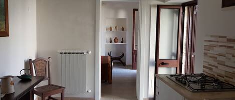 A kitchen with a gas stove, a radiator, a dining table with chairs, and a wooden chair.