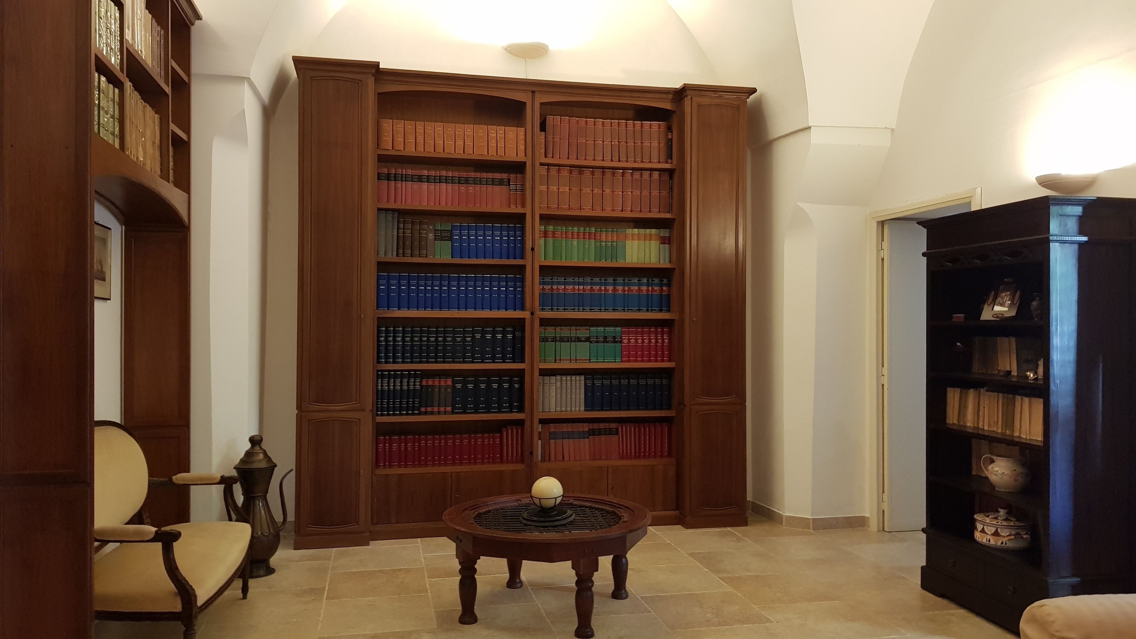 A library with tall wooden bookshelves filled with books, a round wooden table with a globe, and a chair.