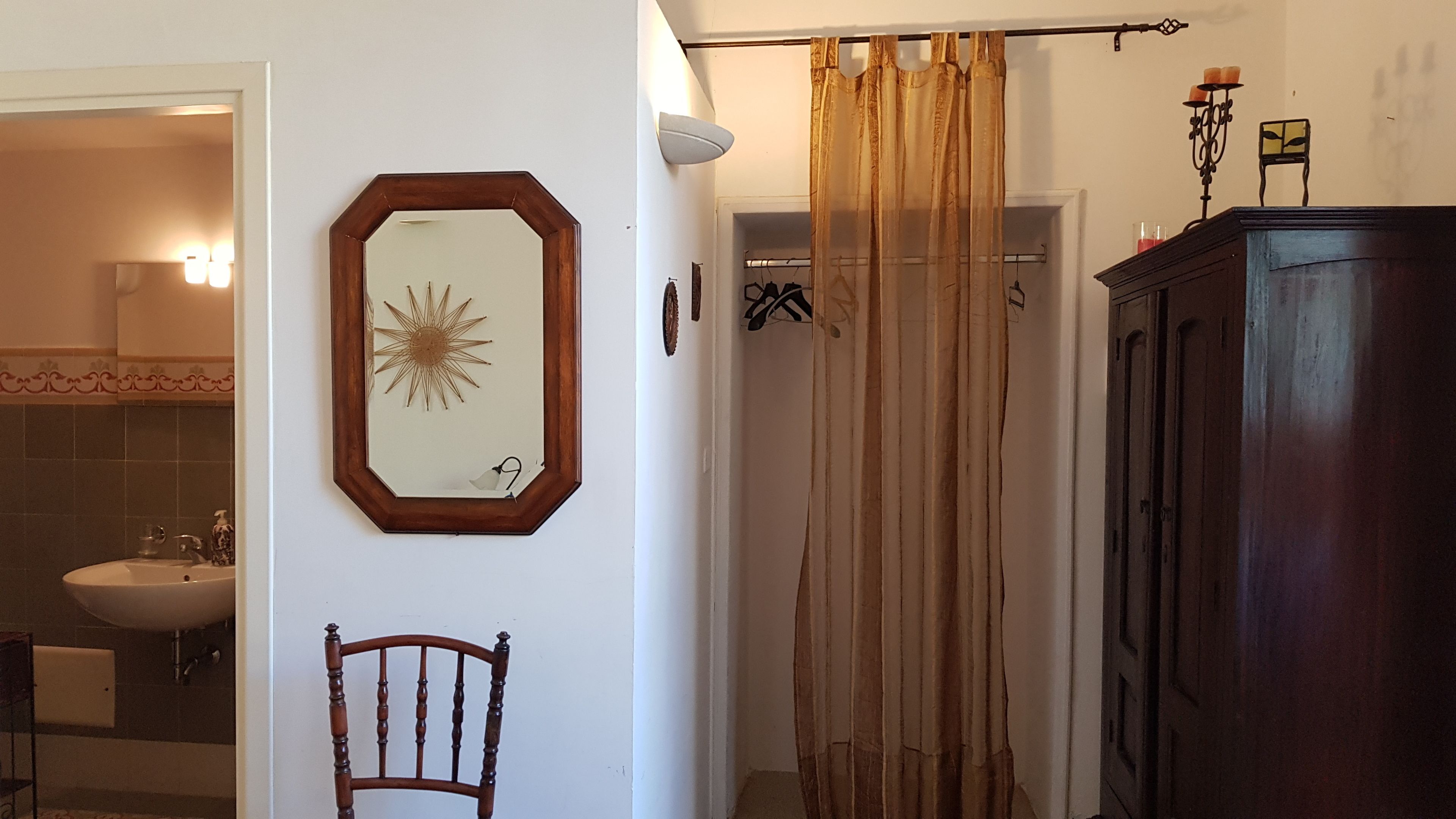 A bathroom with a wooden cabinet, a mirror with a sunburst decoration, a chair, and a shower curtain.