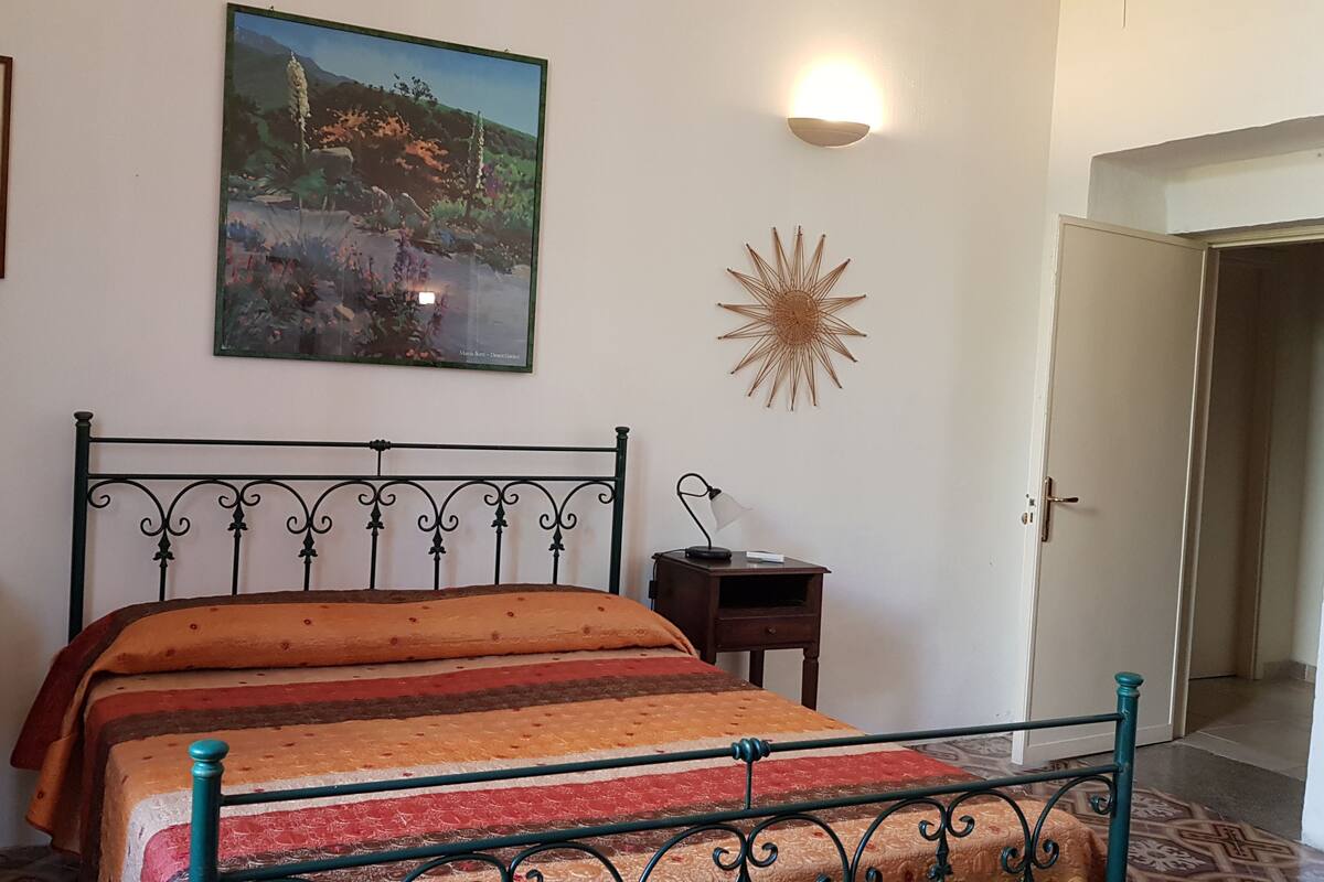 A bedroom with a bed, a nightstand, a wall-mounted lamp, a framed painting, and a decorative star.