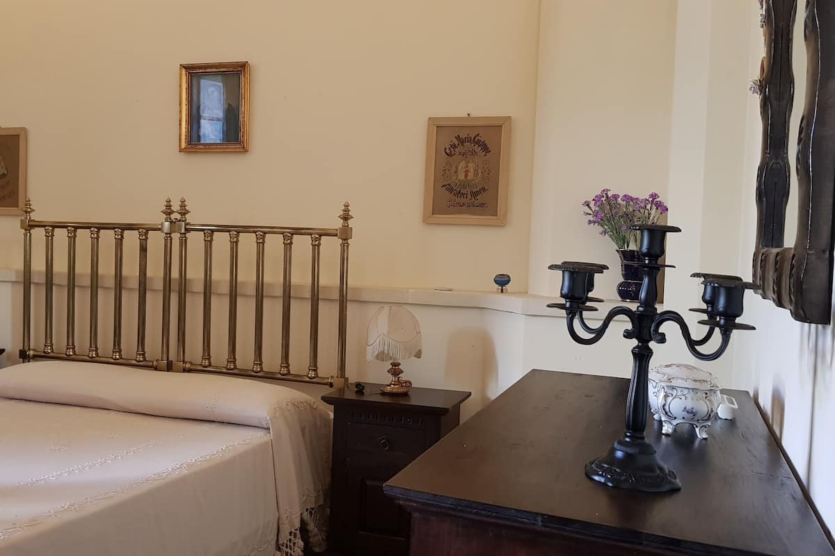 A bedroom with a bed, a nightstand, a dresser, a candelabra, and framed pictures on the wall.