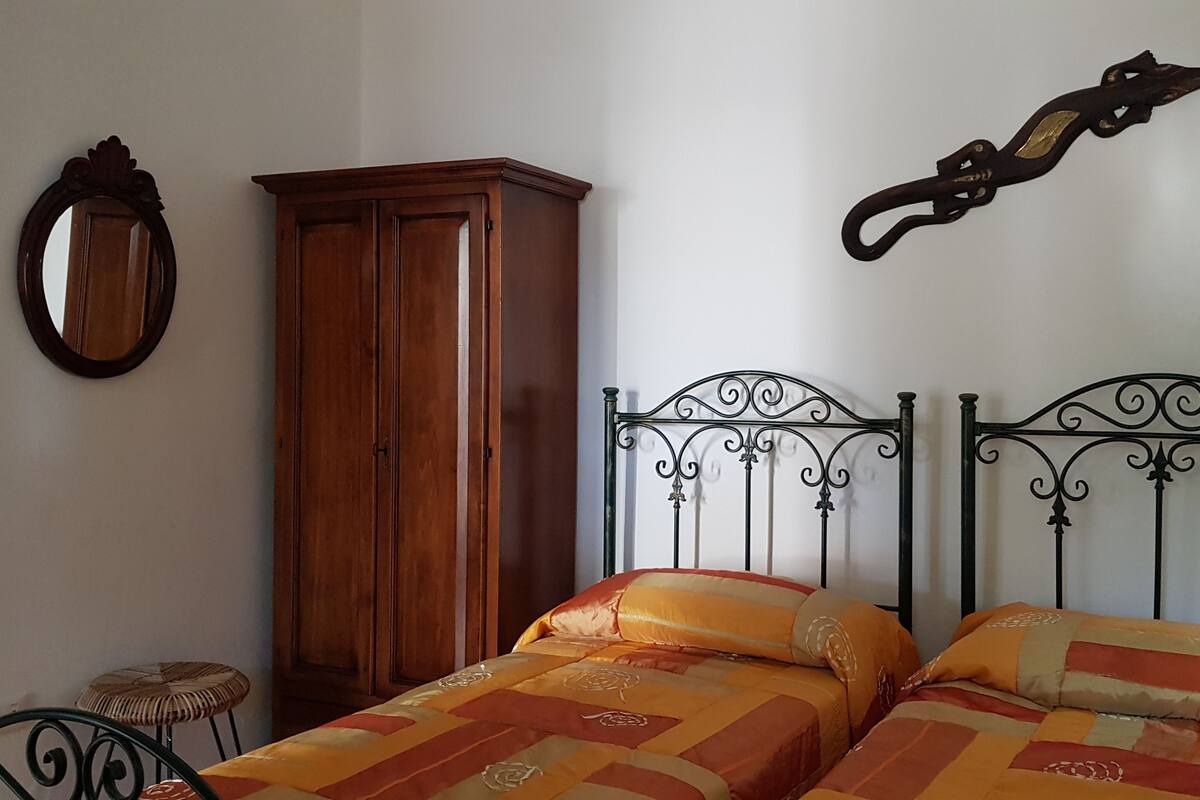 A bedroom with a wooden wardrobe, a metal bed frame, and a mirror on the wall.