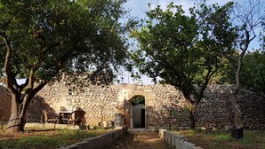 A stone archway leading to a building with a door, surrounded by trees and a stone wall. - B&B Le Due Corti (Martignano)
