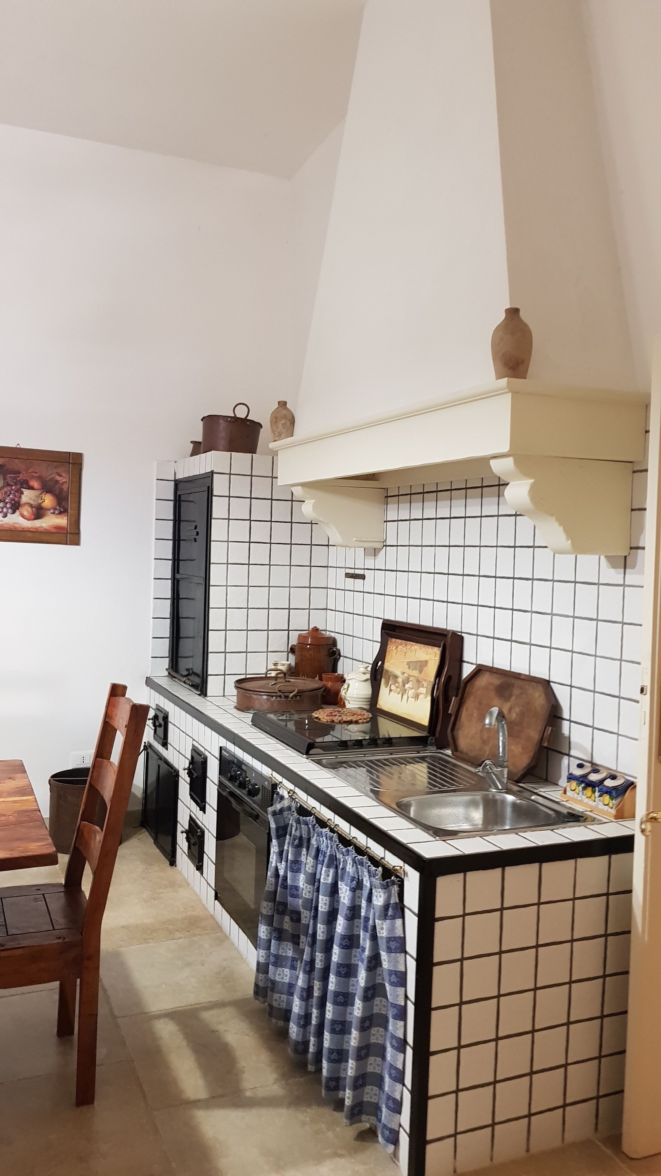 A kitchen with white tiled walls, a wooden table, a hanging pot rack, and a stove.
