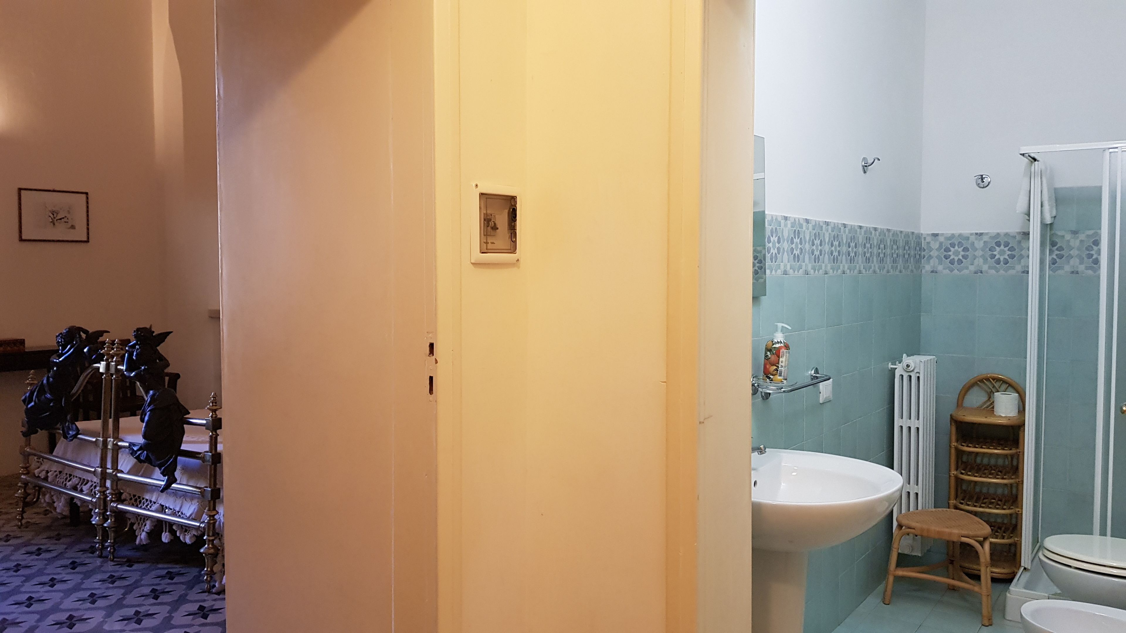 Baño con lavamanos, inodoro y ducha. Incluye una silla y un estante con artículos de aseo.
