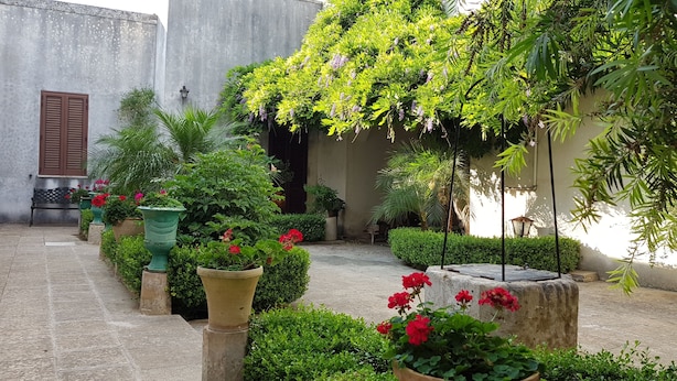 A courtyard with a bench, potted plants, and a variety of greenery. - B&B Le Due Corti (Martignano)