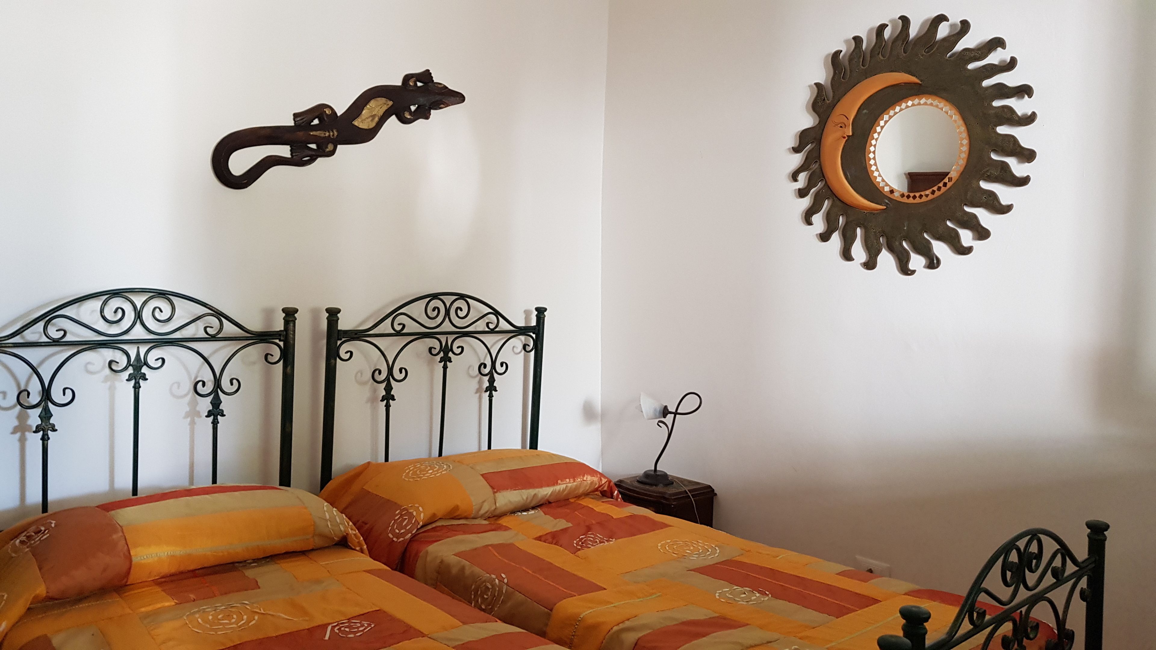 Ein Bett mit Metallgestell und zwei Kissen, ein an der Wand befestigter Spiegel und ein dekoratives Metallkunstwerk darüber.