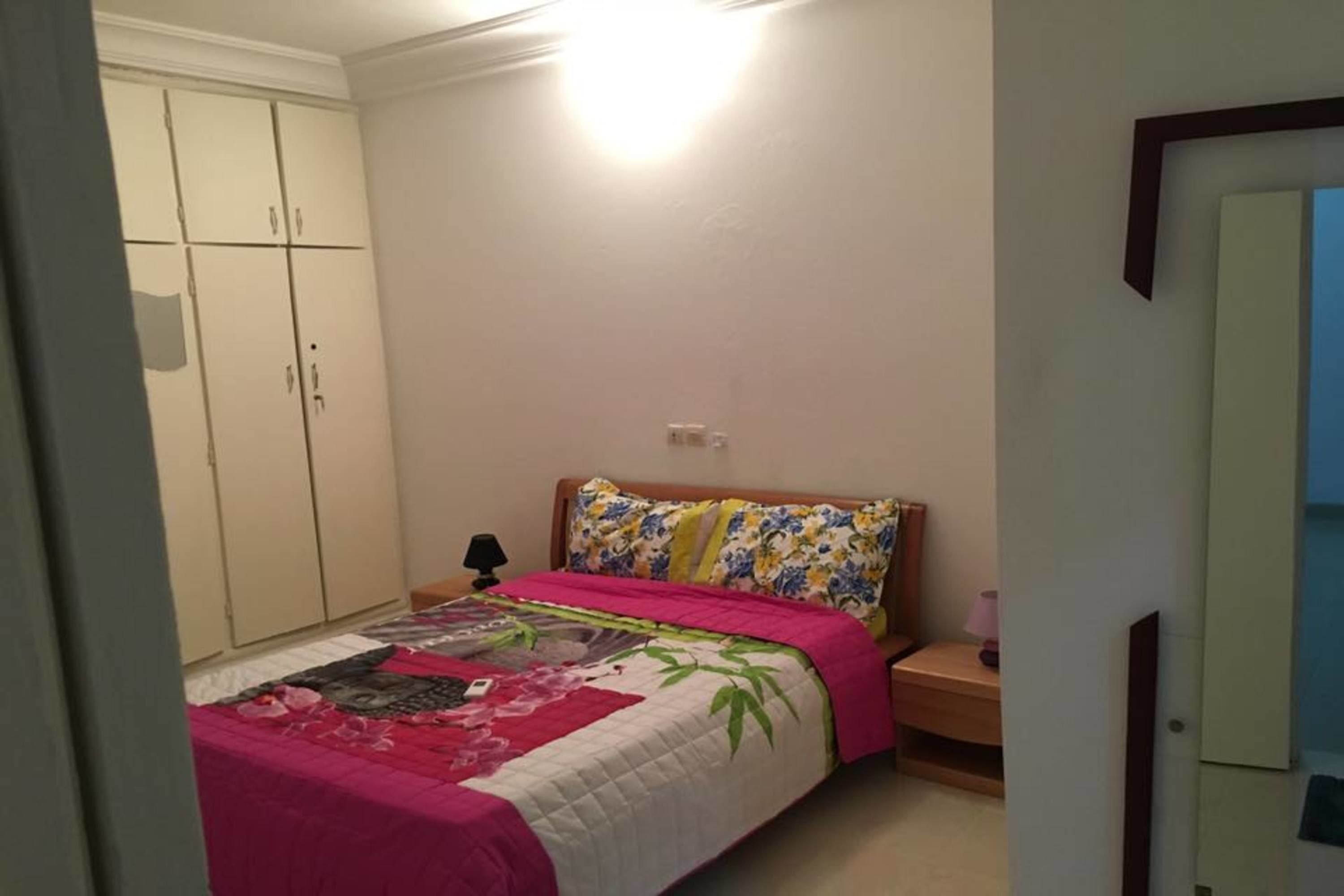Een slaapkamer met een bed, nachtkastje, kledingkast en een wandlamp.