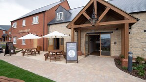 A brick building with a sign reading "Paisley Pear." There are outdoor tables and umbrellas, and a signboard with the text "Welcome to Paisley Pear." - Paisley Pear, Brackley by Marston's Inns (Brackley)