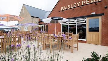 Un espace extérieur aménagé avec des tables et des chaises en bois, des fleurs violettes et des parasols, chez Paisley Pear.