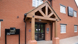 A brick building with a wooden entrance canopy and signs indicating a hotel reception and a pub. - Paisley Pear, Brackley by Marston's Inns (Brackley)