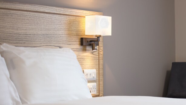 A hotel room with a wooden headboard, a bedside lamp, and a white bed. - Paisley Pear, Brackley by Marston's Inns (Brackley)