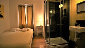 A hotel room with a bed, a nightstand, a lamp, a glass shower enclosure, and a sink.