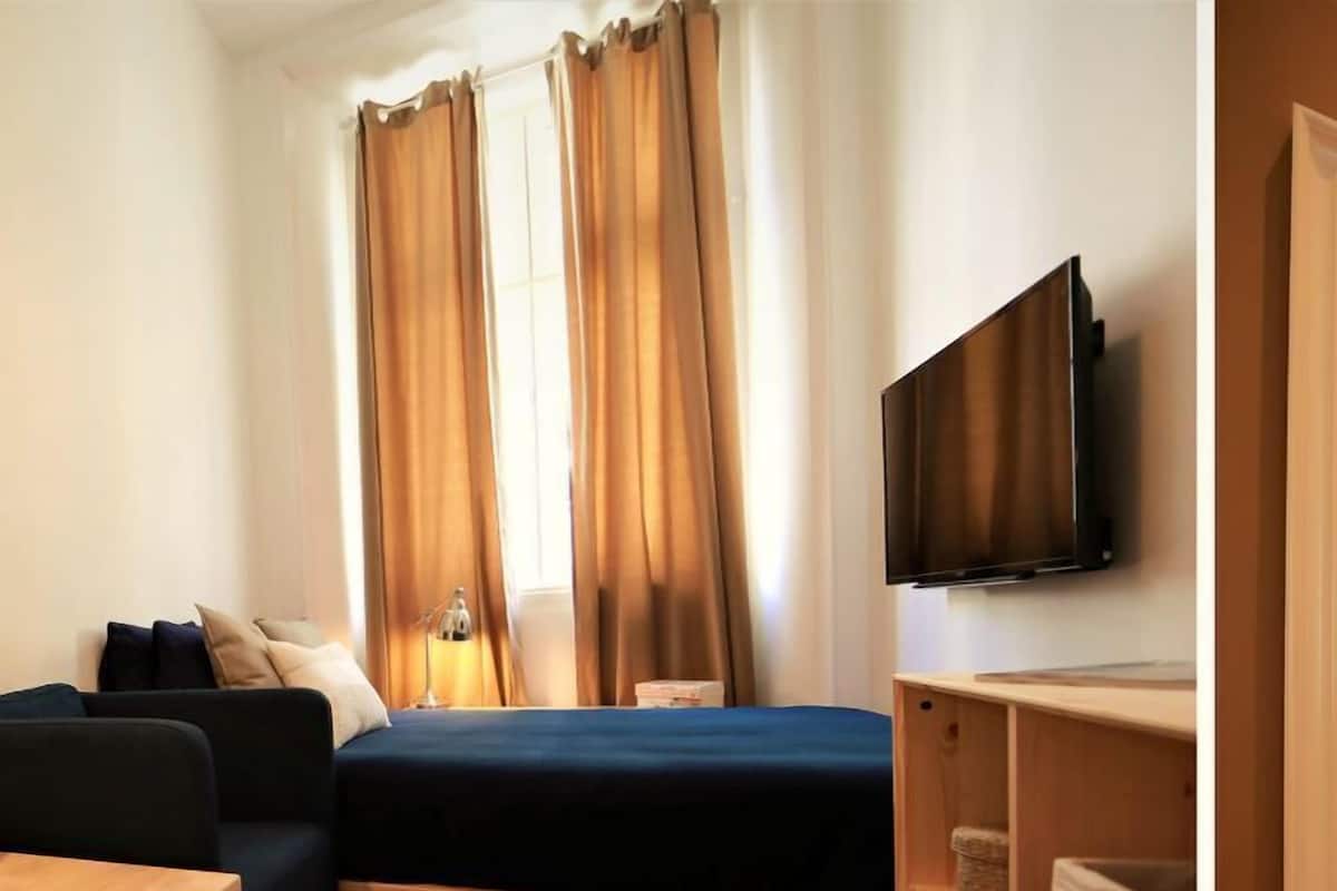 Une chambre à coucher de taille réduite, comprenant un lit, une télévision, une petite table et un canapé.