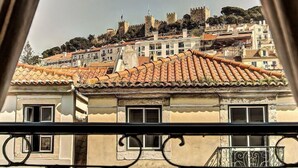 A view of a historic cityscape with a prominent castle on a hill, terracotta-roofed buildings, and a balcony railing in the foreground.