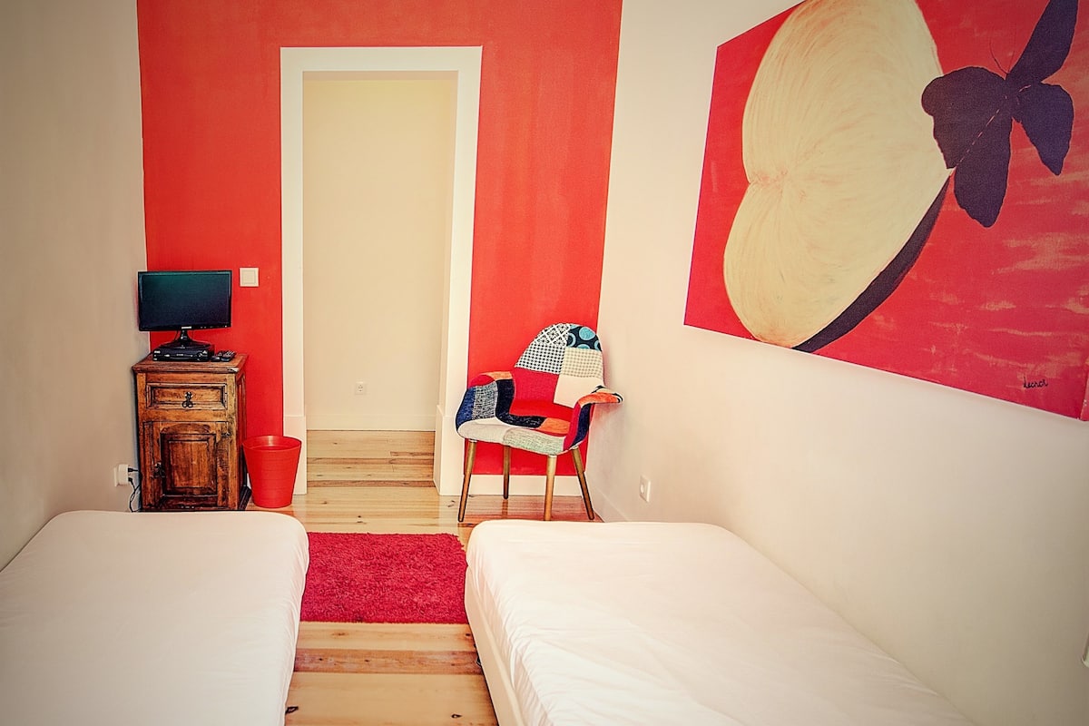 Une chambre avec deux lits simples, un bureau avec un ordinateur, une chaise et un tapis rouge.