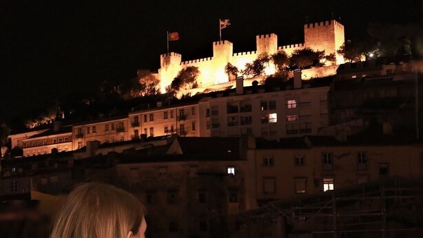 A person sitting by a window overlooking a castle at night.