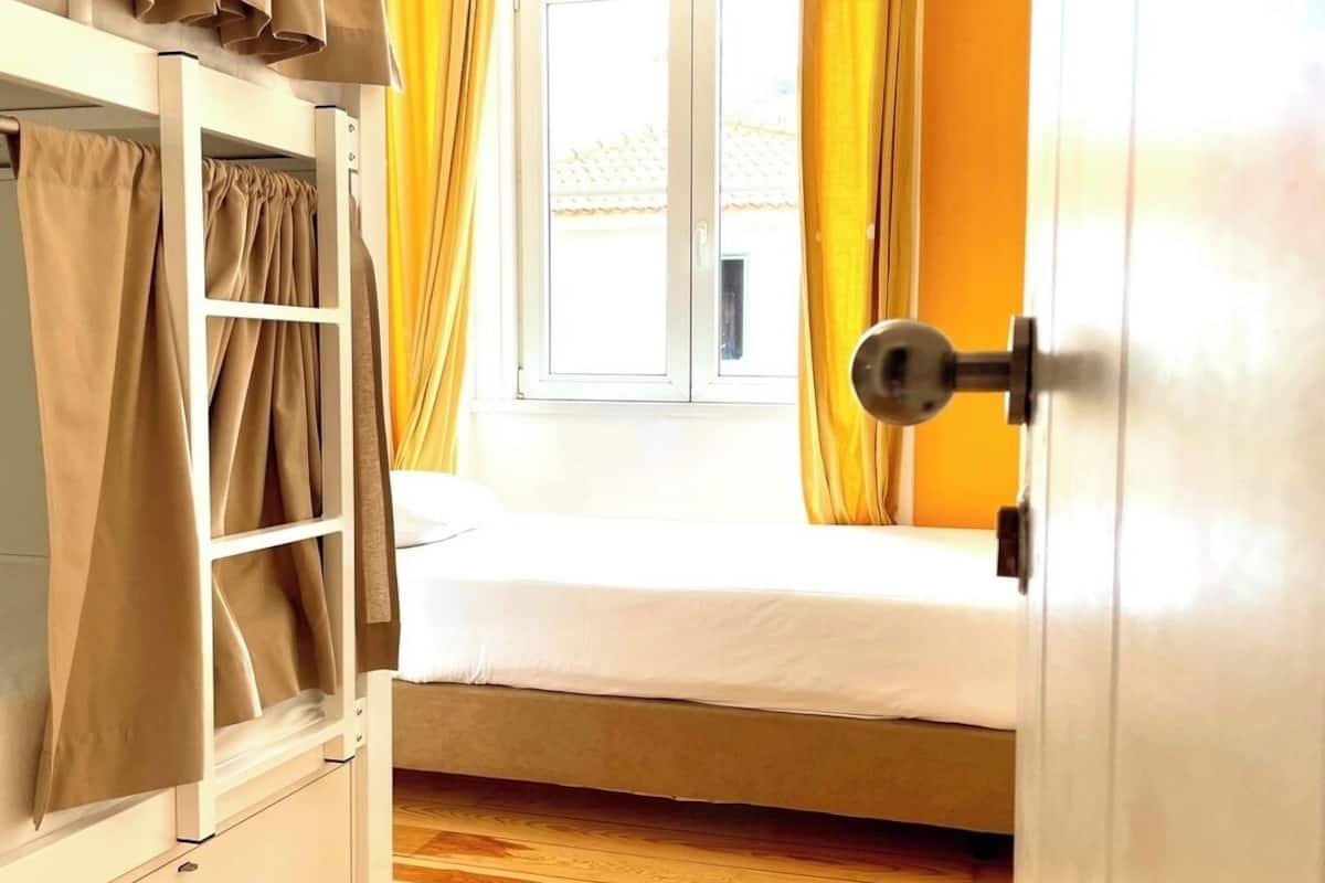Une chambre avec un lit superposé, une fenêtre avec des rideaux jaunes et un plancher en bois.