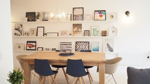 A dining area with a wooden table, four chairs, and a chandelier. The wall behind features a variety of framed artwork and decorative items. - Tincroft Cottage Luxury Coastal Living (Truro)
