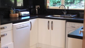 A modern kitchen with white cabinets, a dishwasher, a toaster, and a sink. - Tincroft Cottage Luxury Coastal Living (Truro)