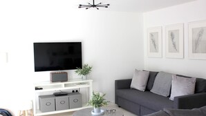 A modern living room with a flat-screen TV, grey sofa, and a coffee table. - Tincroft Cottage Luxury Coastal Living (Truro)