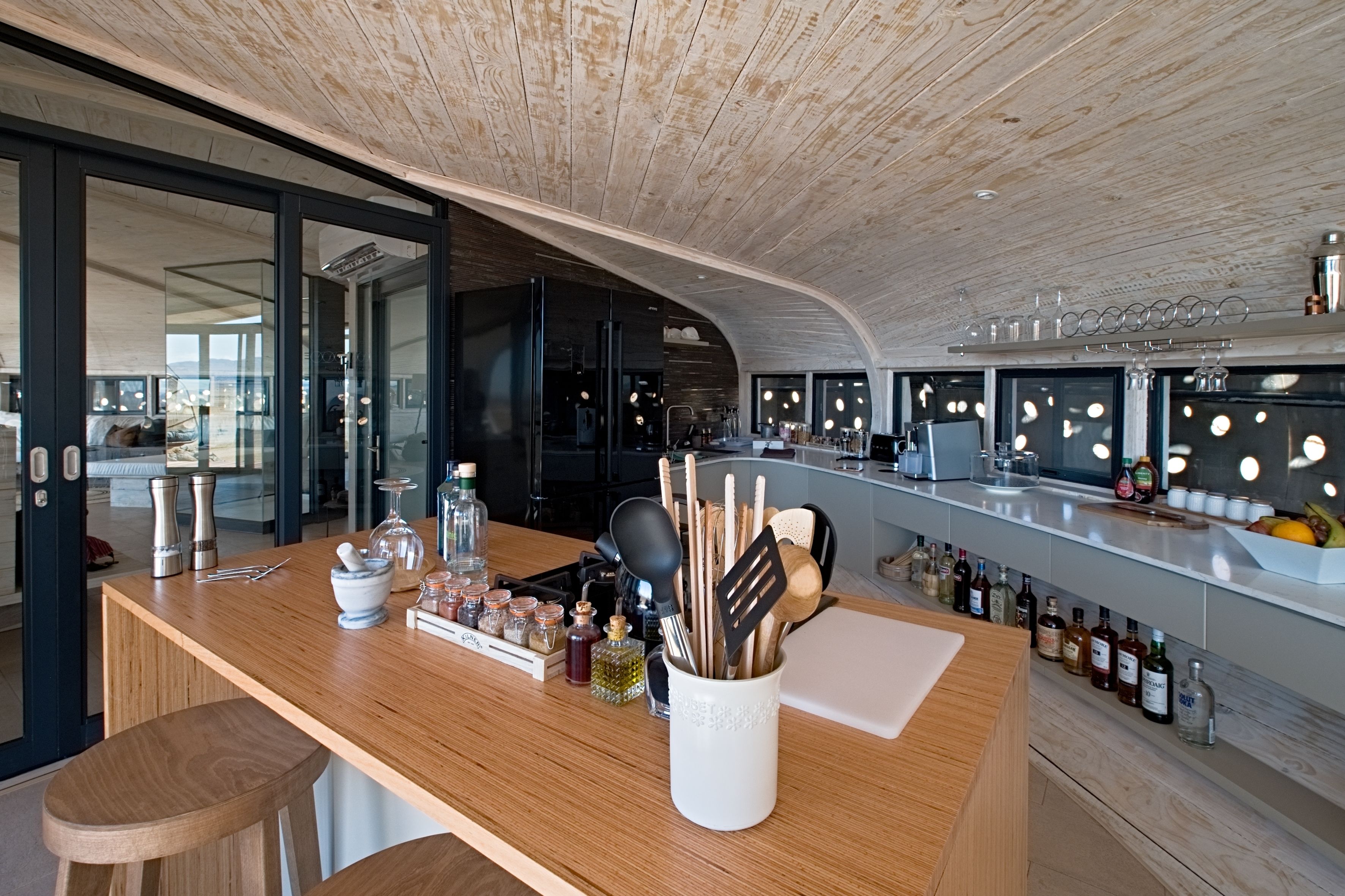 A modern kitchen with a wooden countertop, bar stools, and a variety of kitchen utensils and bottles.