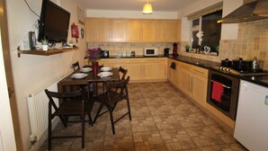 A kitchen with wooden cabinets, a dining table with chairs, a microwave, and a stove. - Atchison Gardens (Derby)