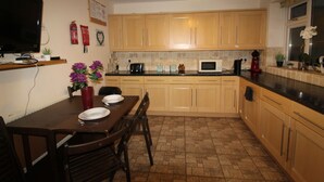 A kitchen with wooden cabinets, a dining table with chairs, a TV, and various kitchen appliances. - Atchison Gardens (Derby)