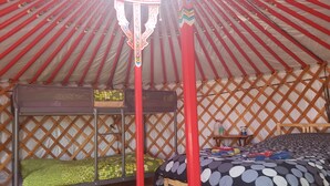 A yurt with two bunk beds, a small table with a water bottle, and a patterned rug. - Flying moose yurt at Cabot Shores Wilderness Resort (Englishtown)