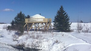 A wooden structure with a dome on top, surrounded by snow and trees. - Flying moose yurt at Cabot Shores Wilderness Resort (Englishtown)