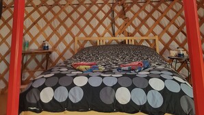 A traditional yurt with a circular roof, a bed with a patterned bedspread, and a wooden lattice wall. - Flying moose yurt at Cabot Shores Wilderness Resort (Englishtown)