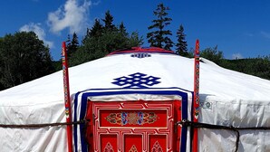 A traditional yurt with a decorative red door, white and blue trim, and a geometric pattern on the lower part. - Flying moose yurt at Cabot Shores Wilderness Resort (Englishtown)