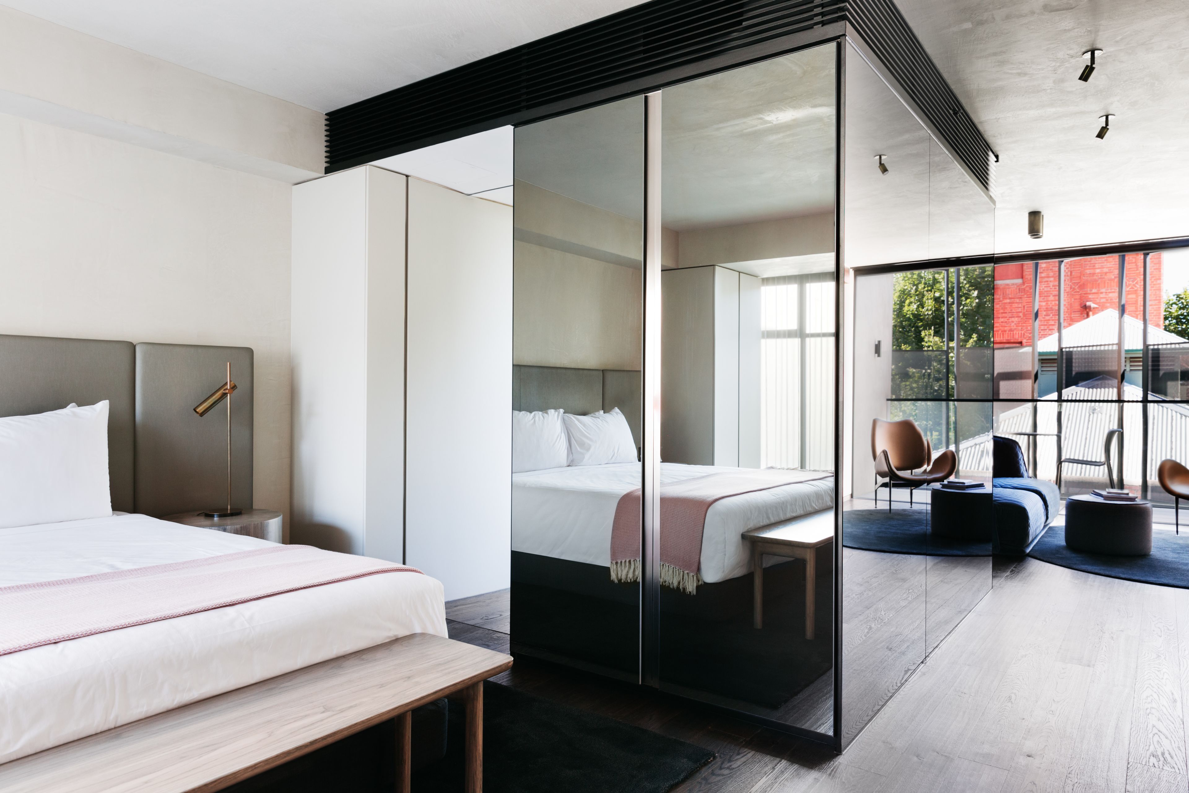 Ein modernes Hotelzimmer mit einem großen Bett, einer separaten Sitzecke mit einer Couch und Sesseln sowie einer Schiebetür zu einem Außenbereich.