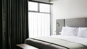 A modern hotel room with a large bed, a bench, and a window with sheer curtains.