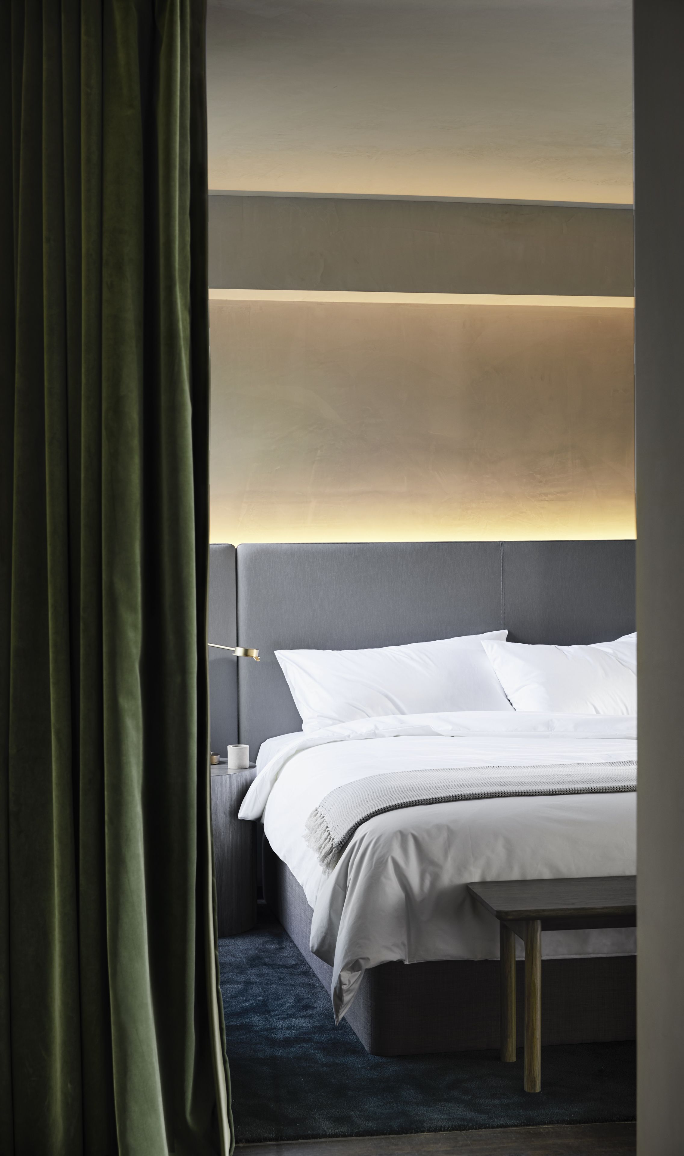 A modern hotel room with a large bed, a bedside table, and a headboard with integrated lighting.