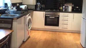 A modern kitchen with white cabinets, a built-in oven, a washing machine, and a coffee maker. - Harvey House (Chesterfield)