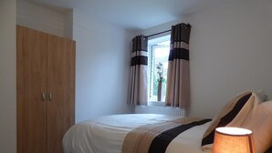 A bedroom with a bed, a nightstand, a wooden wardrobe, and a window with curtains. - Harvey House (Chesterfield)