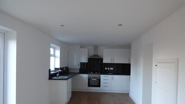 A modern kitchen with white cabinetry, a black backsplash, and a wooden floor. - Harvey House (Chesterfield)
