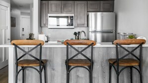 Eine moderne Küche mit grauen Schränken, Edelstahlgeräten und drei Barhocker mit Holzsitzen und Metallgestellen.