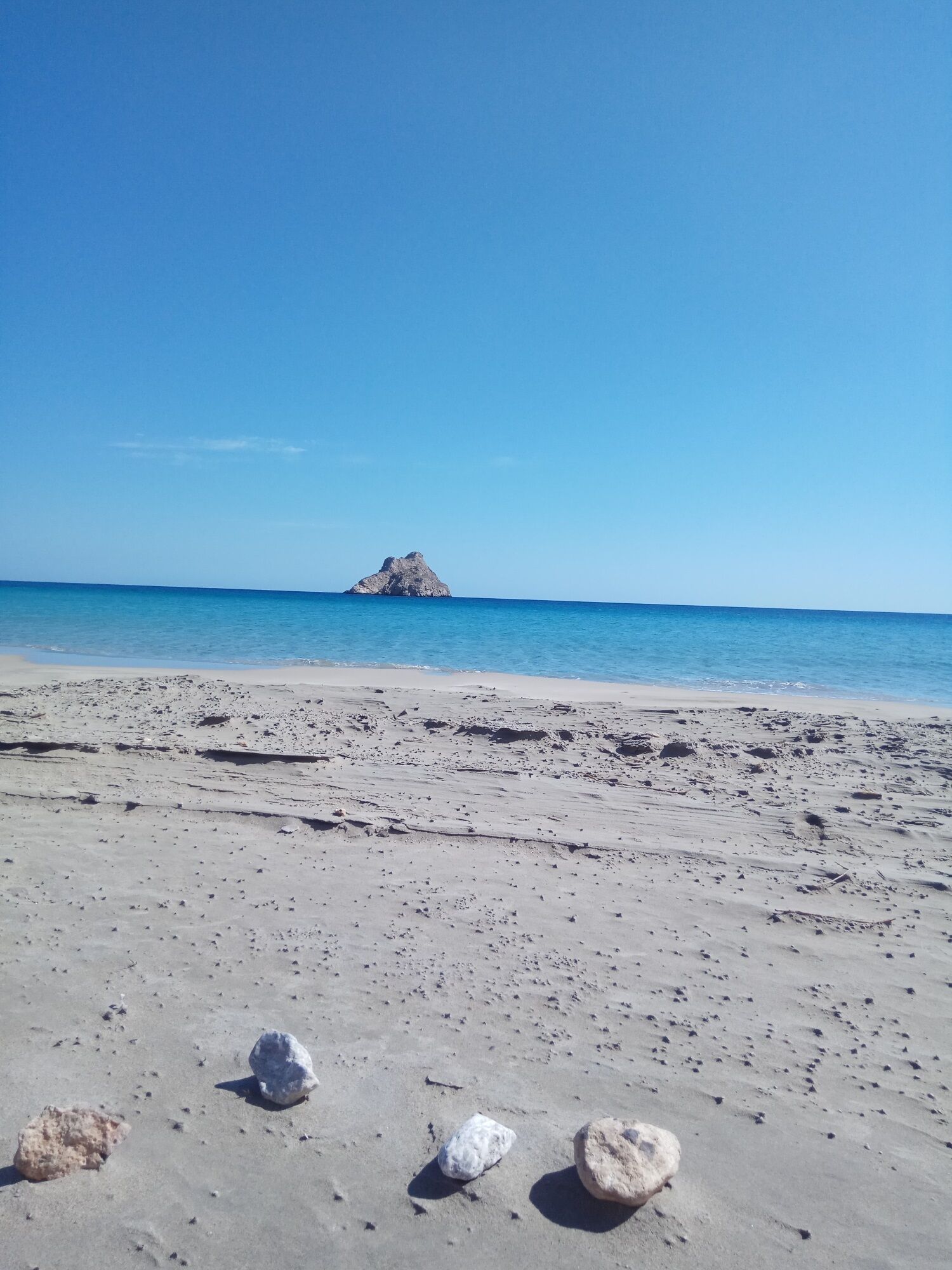 Una playa con tres rocas al frente y una isla en la distancia.