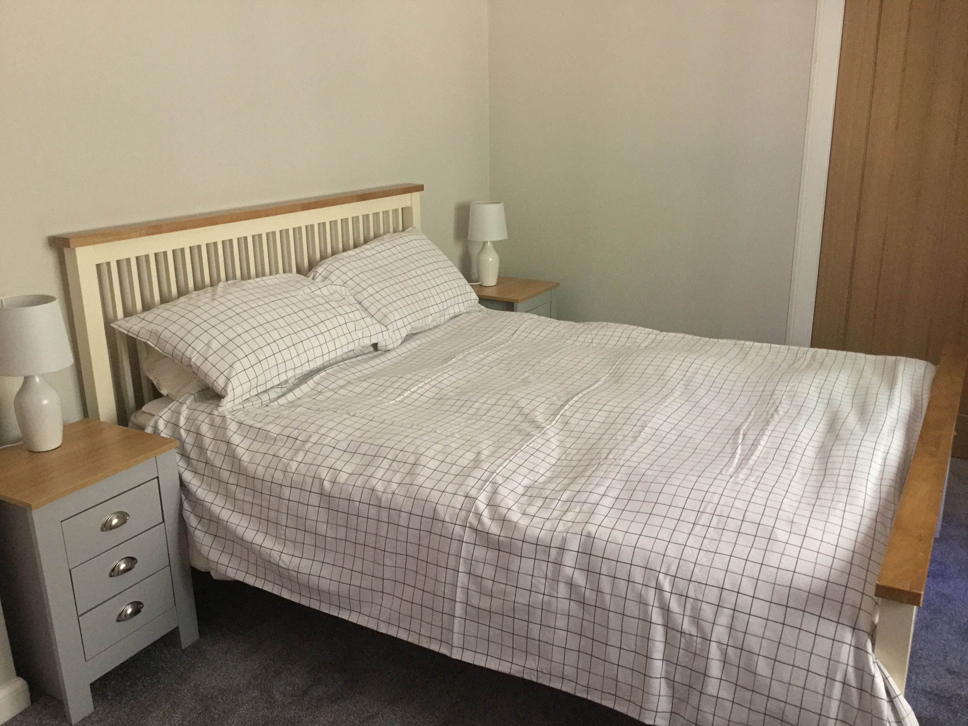 A neatly made bed with a checkered bedspread, a wooden headboard, and two bedside tables with lamps.