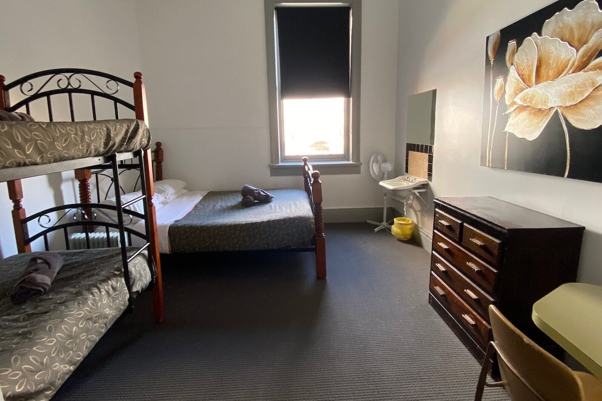 Un dormitorio con literas, una cama individual, una ventana con luz natural, un lavamanos pequeño, un espejo y un aparador.