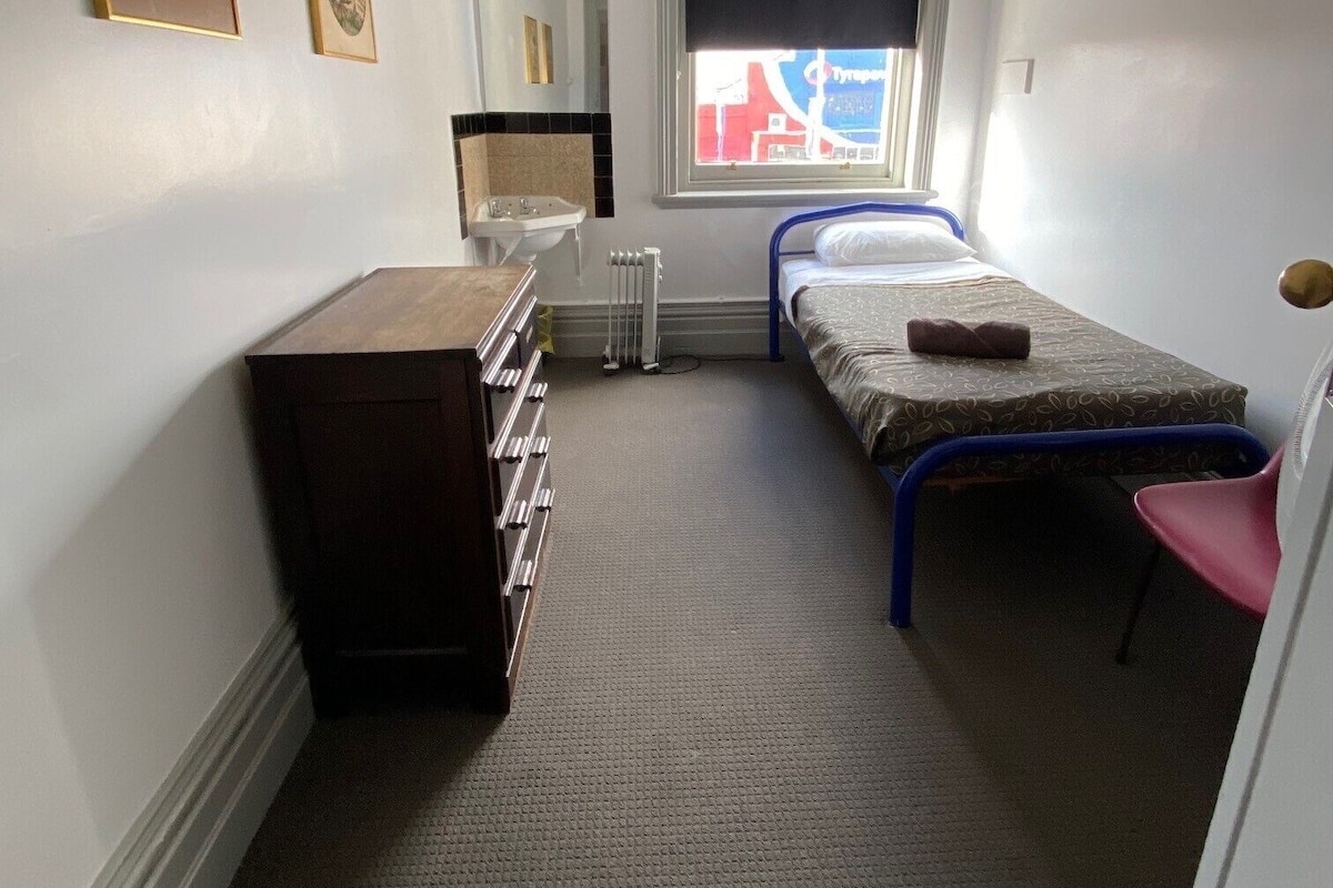 Una habitación pequeña y poco amueblada con una cama individual, un escritorio y una silla.
